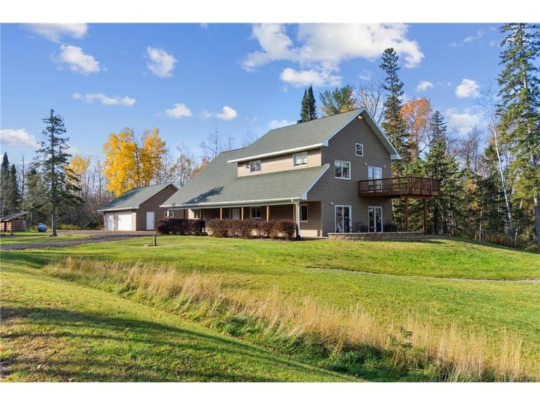 Modern two-story home with green roof on expansive lawn surrounded by evergreen and autumn trees under blue sky