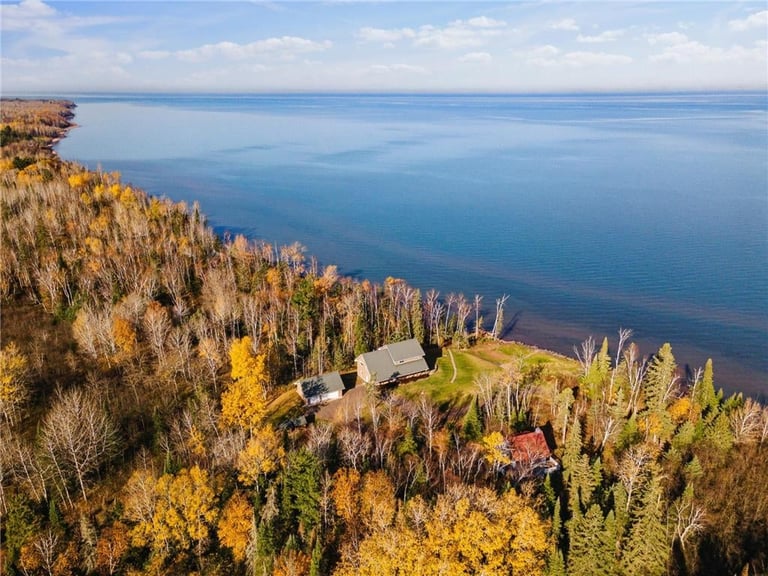 Aerial view of a cottage on a forested shoreline overlooking a calm blue lake in autumn