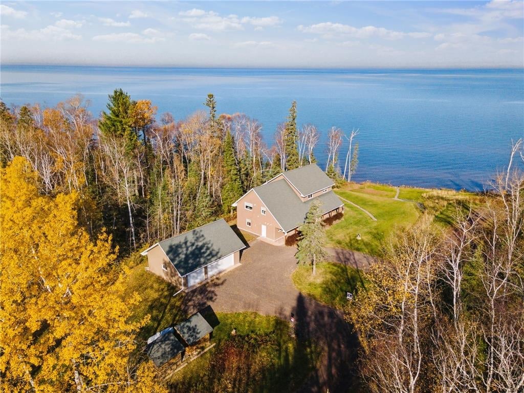 Aerial view of a residential house surrounded by autumn trees overlooking a large blue lake